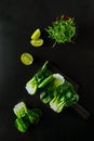 Baby bok choi halves, lime wedges, green sprouts on black background. Top view, vertical orientation Royalty Free Stock Photo