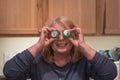 Baby boomer woman holds two mini frosted cupcakes up to her eyes, as glasses, acting silly