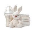 Baby bottle with milk, bunny toy and stack of diapers on white background