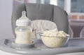 A baby bottle with milk and a plate with dry milk formula enriched with bifidobacteria, vitamins and minerals stands