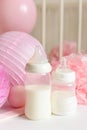 Baby bottles with breast milk with various festive paper decor and balloons in front of baby bedroom. It`s a girl or baby birthda