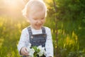 Baby with bouquet of flowers in the garden in sunlight. Cute happy summer blond girl in the garden. Apple blossom Royalty Free Stock Photo