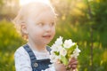 Baby with bouquet of flowers in the garden in sunlight. Cute happy summer blond girl in the garden. Apple blossom Royalty Free Stock Photo