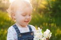 Baby with bouquet of flowers in the garden in sunlight. Cute happy summer blond girl in the garden. Apple blossom Royalty Free Stock Photo