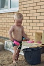 Baby boy with blonde hair plays in the yard of the house in the sand with water.