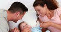 Baby boy in blue babygro being tickled by happy parents on bed