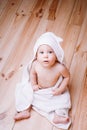 Baby boy with brown eyes is five months old wrapped in a white towel with ears on wooden background . Royalty Free Stock Photo