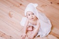 Baby boy with brown eyes is five months old wrapped in a white towel with ears on wooden background . Royalty Free Stock Photo