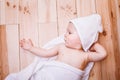 Baby boy with brown eyes is five months old wrapped in a white towel with ears on wooden background . Royalty Free Stock Photo