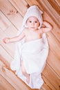 Baby boy with brown eyes is five months old wrapped in a white towel with ears on wooden background . Royalty Free Stock Photo