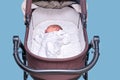 Baby boy in a carriage on a blue background. A child in white clothes in only diapers is lying in a stroller, studio shot Royalty Free Stock Photo