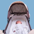 Baby boy in a carriage on a blue background. A child in white clothes in only diapers is lying in a stroller, studio shot Royalty Free Stock Photo