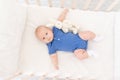 A baby boy in a crib lies on his back with a toy, a happy newborn wakes up in the morning or goes to bed Royalty Free Stock Photo