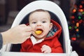 Baby boy with dark black eyes sitting in high chair in kitchen looking in camera eating meal puree Royalty Free Stock Photo