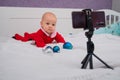 A baby boy dressed in a Santa suit sits on the bed and looks at the sick phone. Christmas greetings by video call Royalty Free Stock Photo