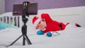 A baby boy dressed in a Santa suit sits on the bed and looks at the sick phone. Christmas greetings by video call Royalty Free Stock Photo