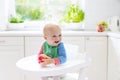 Baby boy eating apple in white kitchen at home Royalty Free Stock Photo