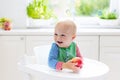 Baby boy eating apple in white kitchen at home Royalty Free Stock Photo