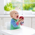 Baby boy eating apple in white kitchen at home Royalty Free Stock Photo