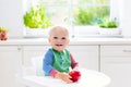 Baby boy eating apple in white kitchen at home Royalty Free Stock Photo