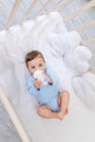 Baby boy eating from milk bottle in crib in blue bodysuit, cute little baby in bedroom, baby food concept Royalty Free Stock Photo