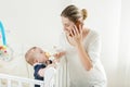 Cute baby boy eating milk from bottle and looking at mother talking by phone Royalty Free Stock Photo