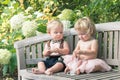 Baby boy and girl in formal dress sitting on wooden bench in a beautiful garden Royalty Free Stock Photo