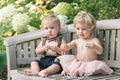 Baby boy and girl in formal dress sitting on wooden bench in a beautiful garden Royalty Free Stock Photo