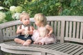 Baby boy and girl in formal dress sitting on wooden bench in a beautiful garden Royalty Free Stock Photo