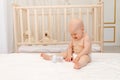 Baby boy 8 months old sitting in diapers on a white bed with a bottle of milk at home and crying, baby food concept, first bait, Royalty Free Stock Photo
