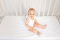 Baby boy 8 months old sitting in a crib in a children`s room in white clothes and looking at the camera, the morning of the baby Royalty Free Stock Photo