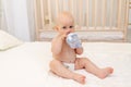 Baby boy 8 months old sitting in diapers on a white bed with a bottle of milk at home, baby food concept, first bait, place for Royalty Free Stock Photo