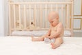 Baby boy 8 months old sitting in diapers on a white bed with a bottle of milk at home, baby food concept, first bait, place for Royalty Free Stock Photo