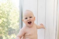 Baby boy 8 months old sitting in diapers on the window sill and looking into the distance, a place for text Royalty Free Stock Photo