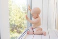 Baby boy 8 months old sitting in diapers on the window sill and looking into the distance, a place for text Royalty Free Stock Photo