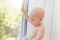 Baby boy 8 months old sitting in diapers on the window sill and looking into the distance, a place for text Royalty Free Stock Photo