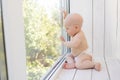 Baby boy 8 months old sitting in diapers on the window sill and looking into the distance, a place for text Royalty Free Stock Photo