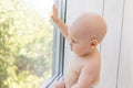 Baby boy 8 months old sitting in diapers on the window sill and looking into the distance, a place for text Royalty Free Stock Photo