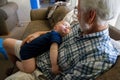 Baby Boy in a Onsie Passed Out Asleep on the Chest of his Grandfather Who is Looking at his Grandson