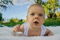 A baby boy outdoors in a green forest crawling on grass on a white blanket