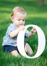 Baby boy playing with big white letter O sitting on green grass at summer day