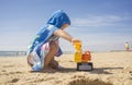 Baby boy playing on sand at the beach with excavator toy