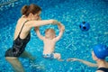 Baby boy running to ball inflatable toy. Coach raising child upright to perform exercise with hands up and feet in water Royalty Free Stock Photo