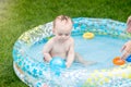 Cute baby boy sitting in inflatable swimming pool and playing with blue ball Royalty Free Stock Photo