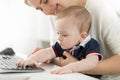 Cute baby boy sitting on mothers lap in office and typing on computer keyboard Royalty Free Stock Photo