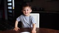 Baby boy sitting at the table and does not want to eat soup, pushing the plate and running away, laughing