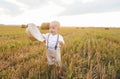 A baby boy with a straw hat walks in the field. Wheat field sunset