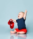 Baby boy in t-shirt and red shorts, barefoot. He smiling, raised hands, holding cap, sitting on floor. Blue background. Close up Royalty Free Stock Photo