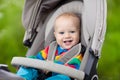 Baby boy in warm colorful knitted jacket sitting in modern stroller on a walk in a park. Child in buggy. Little kid in a pushchair Royalty Free Stock Photo