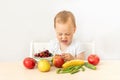 Baby boy 2 years old sitting at a table on a white isolated background and eating fruits vegetables, baby food concept, place for Royalty Free Stock Photo